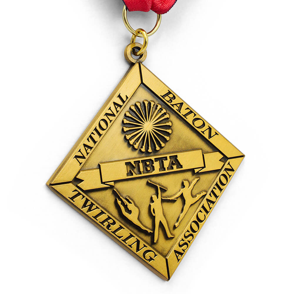 Angled view of unique GUGLE custom medal for awards featuring diamond shape, gold finish, NBTA baton twirling design and flowing red-white-blue ribbon