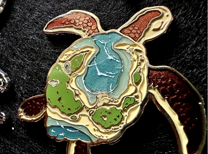 Turtle-shaped enamel pin featuring ocean and island map design, with colorful baked enamel, gold metal outlines, and textured limbs, perfect for custom badges and collectible pins