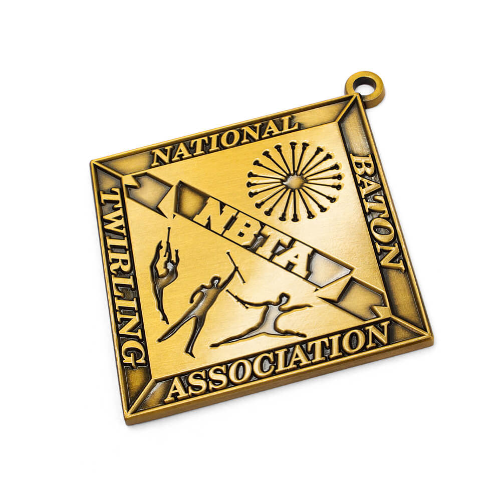 Close-up of GUGLE custom award medal showing gold diamond with NBTA banner, floral emblem, baton twirlers in action poses and detailed engraving