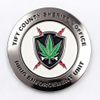 A funny challenge coin showing the Tift County Sheriff's Office emblem, with a cannabis leaf surrounded by a skull, crossbones, and red lightning. The design humorously amplifies the dangers of drugs with a satirical twist, combining law enforcement symbolism with danger and death motifs for a bold, ironic effect.