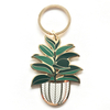Gold-rimmed enamel keychain featuring a lush green houseplant in a woven basket pot