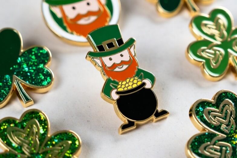 Colorful St. Patrick's Day custom enamel pins featuring leprechaun with pot of gold, four-leaf clovers, and glitter shamrock