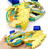 Close-up of GUGLE custom finisher medal showing intricate golden phoenix wings, black-red head, pink flames, swirling clouds and colorful enamel design in turquoise and gold