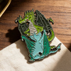 Soft enamel dragon pin with funny green dragon hugging blue dragon on wooden table lifestyle view