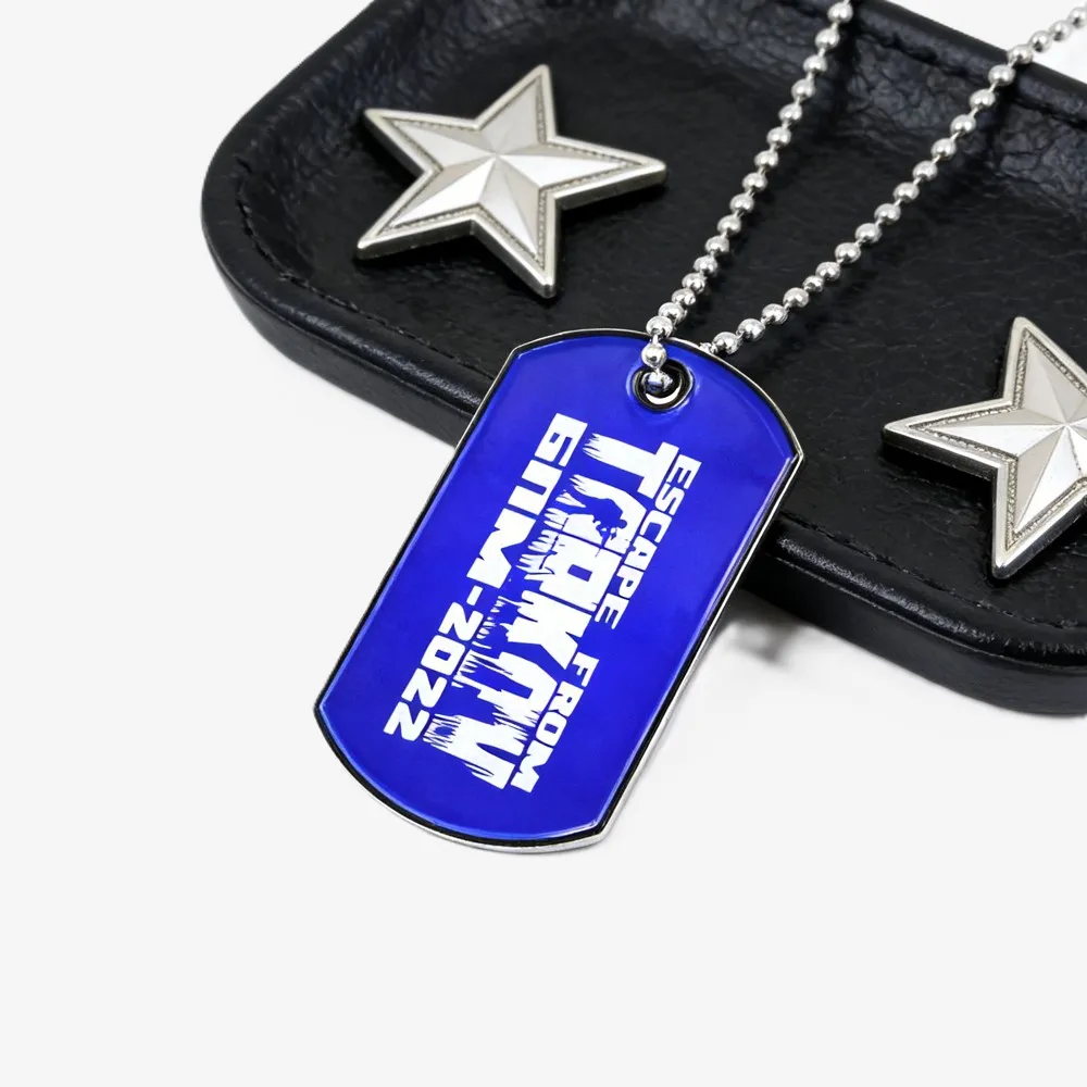 Blue metal dog tag pendant with a ball chain, printed with white “Escape From MUMU 2022” text on a black leather background.